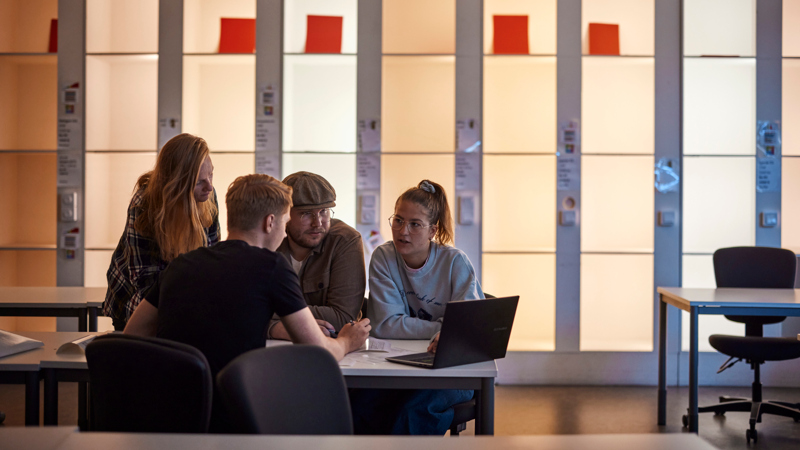 Fyra studenter sitter runt ett bord och diskuterar.