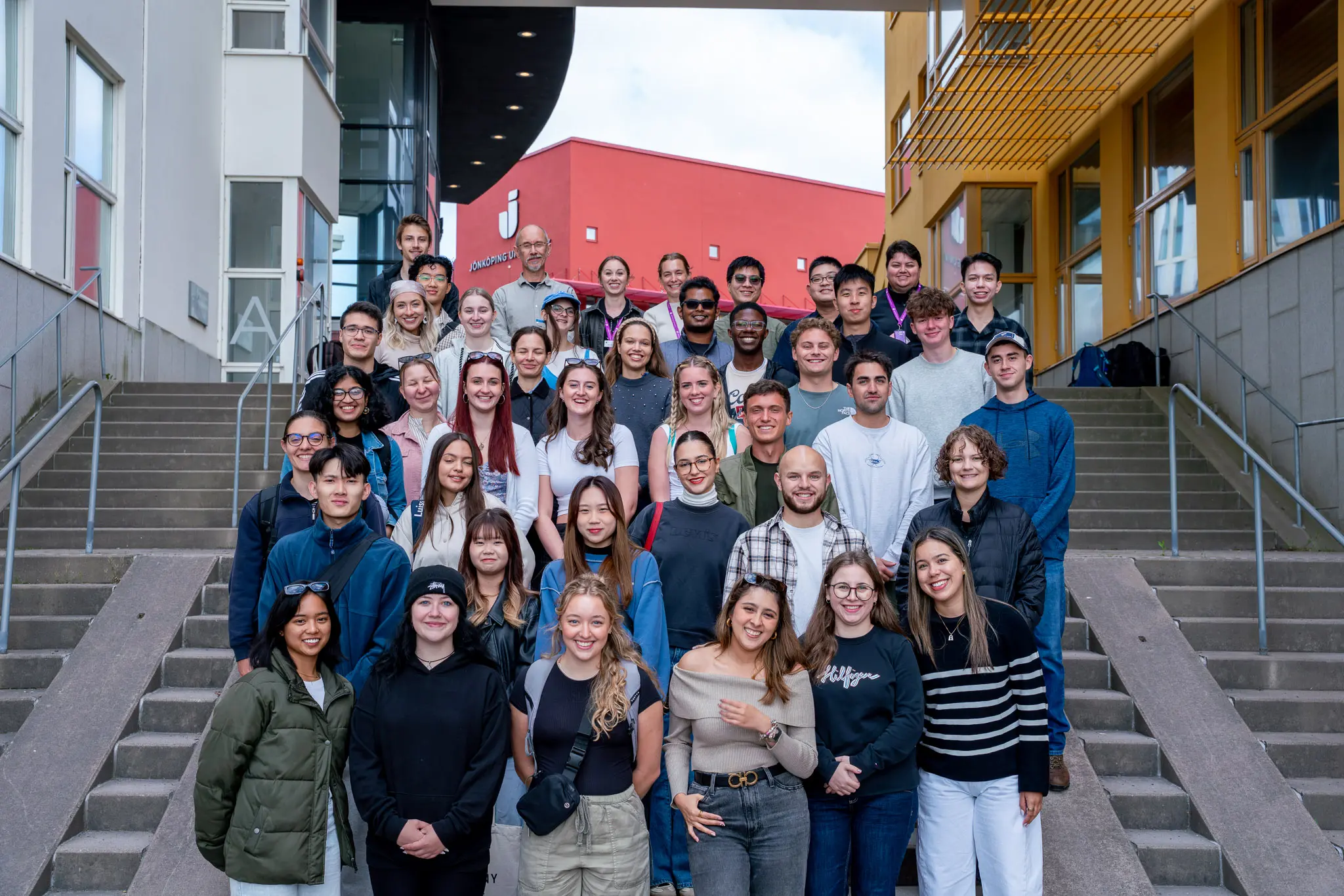 A group of summer students at Jönköping University campus, standing on a staircase and looking into the camera.