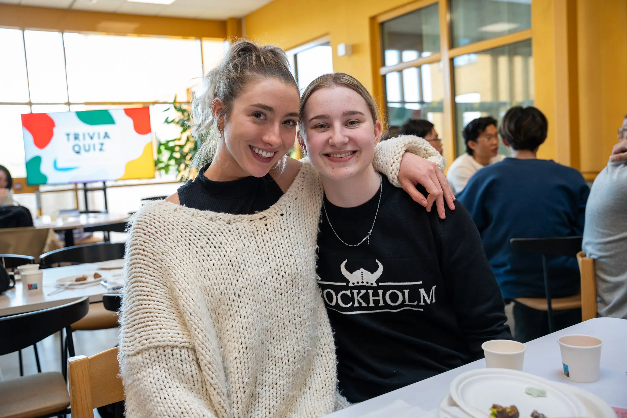 Två tjejer med armen om varandra ler och tittar in i kameran.