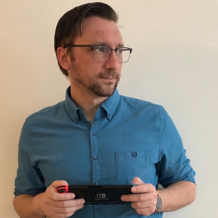 Brian McCauley stands holding a gaming console and looks off to his left. 