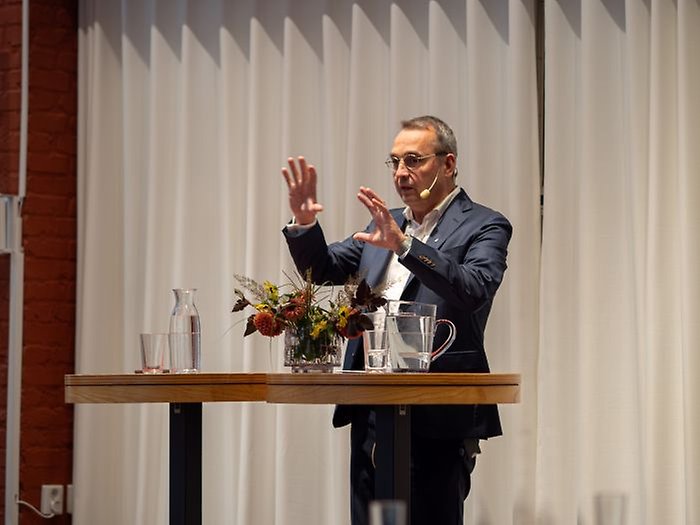 A man standing by a high table, gesticulating with his hands.